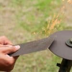 Man sharpening lawn mower blades with angle grinder